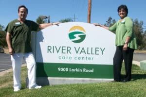 The front entrance sign and two employees at River Valley